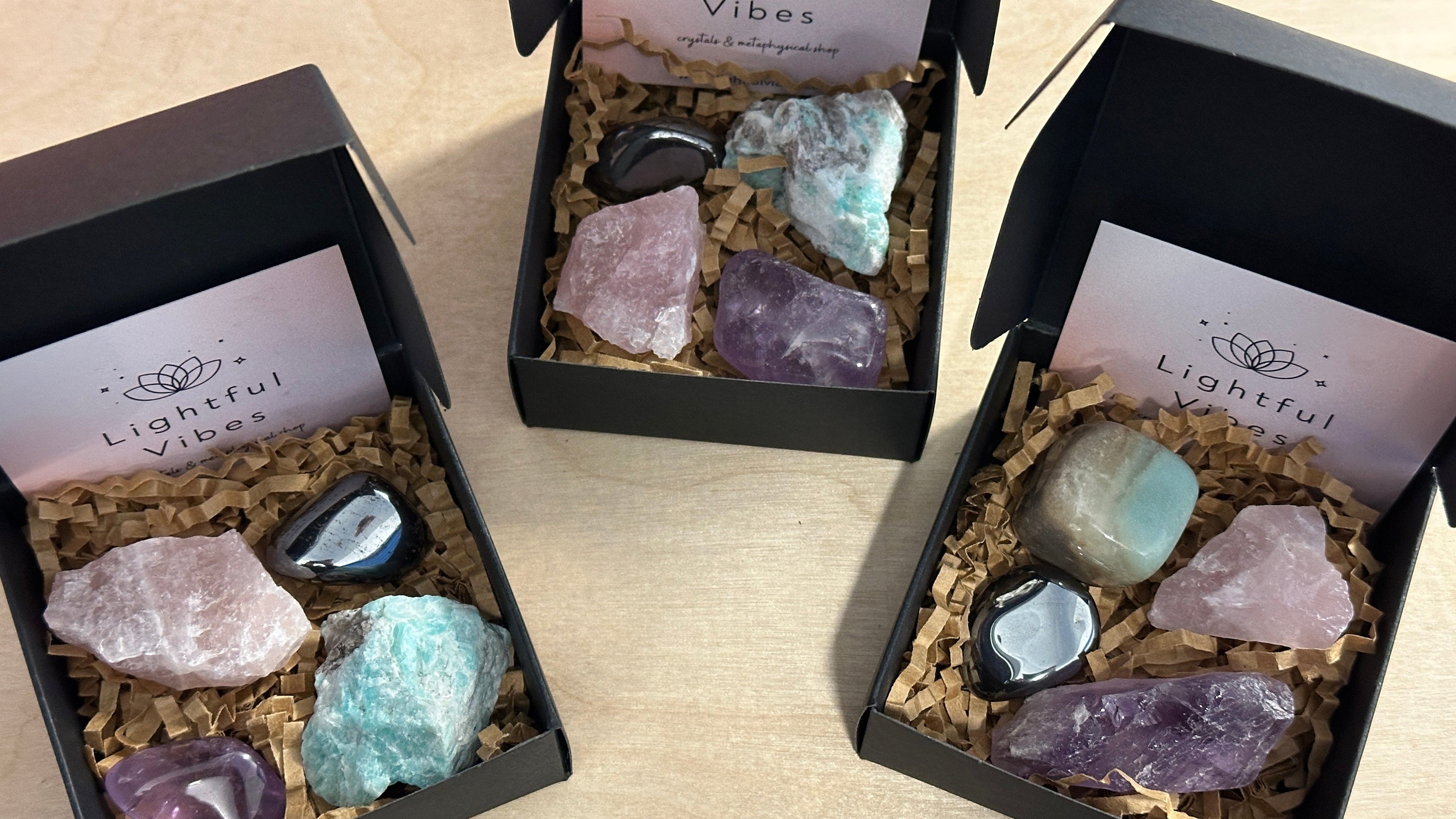 Three boxes of Lightful Vibes containing various crystals on a wooden surface.